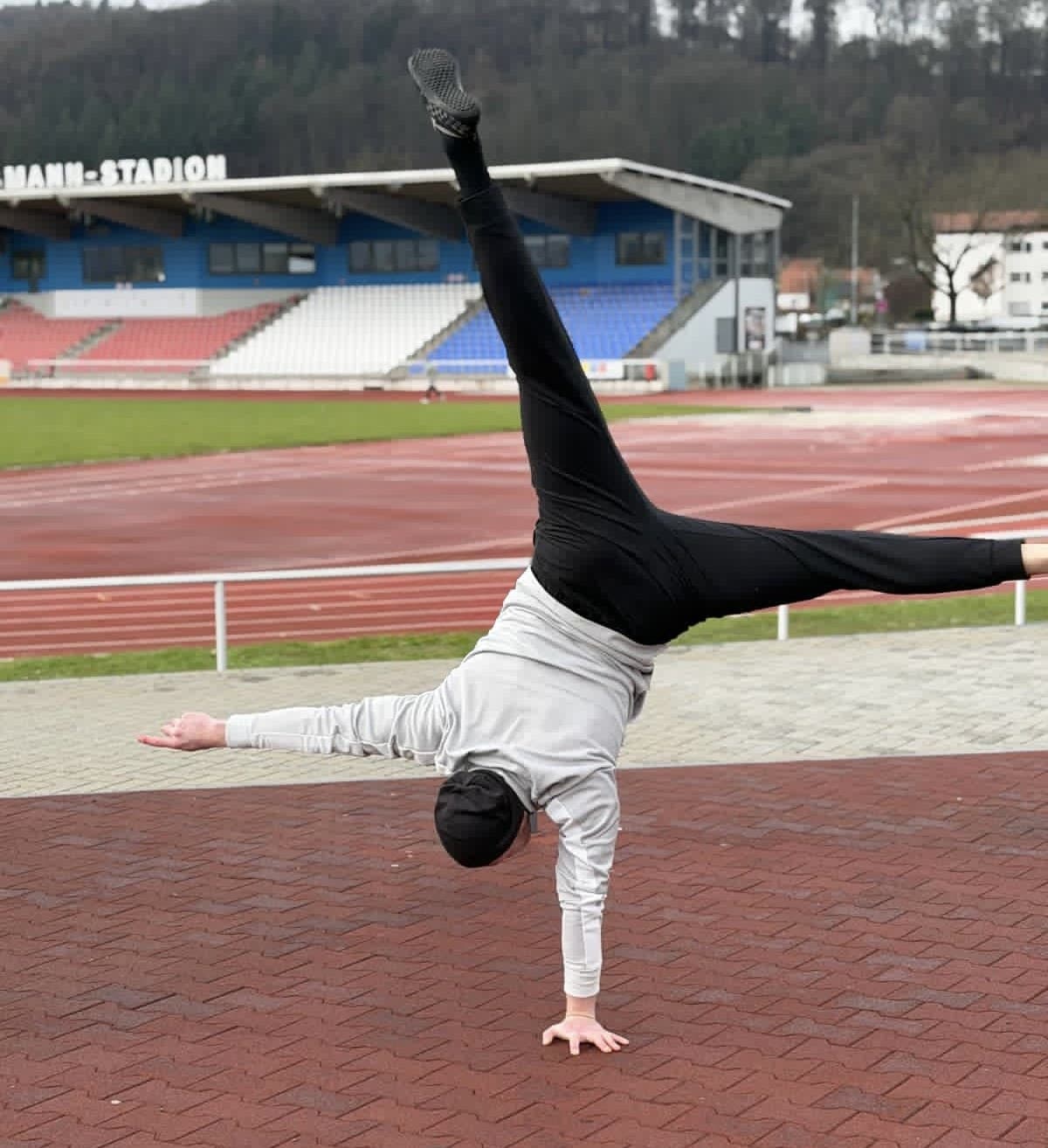 Ruslan Spartakov im einarmigen Handstand vor einem Stadion
